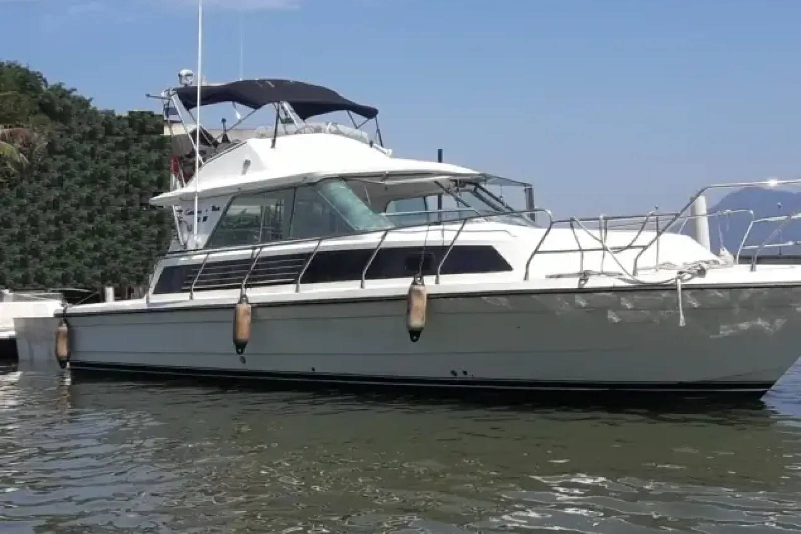 A lancha de pesca Carbrasmar 32, de design clássico com flybridge, parada em águas calmas próximo a uma encosta verde