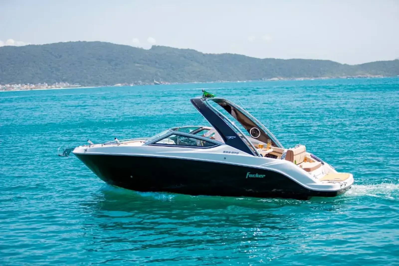 A lancha cabinada Focker 255, com casco escuro e deck branco, navegando em águas azul-turquesa em um dia ensolarado