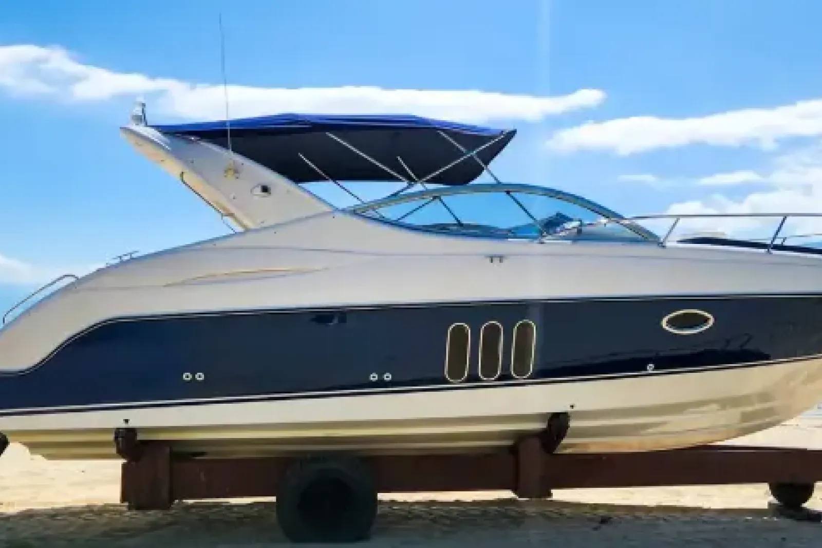 A lancha Phantom 290, com casco azul-escuro e deck branco, apoiada em um suporte de madeira na areia, fora da água