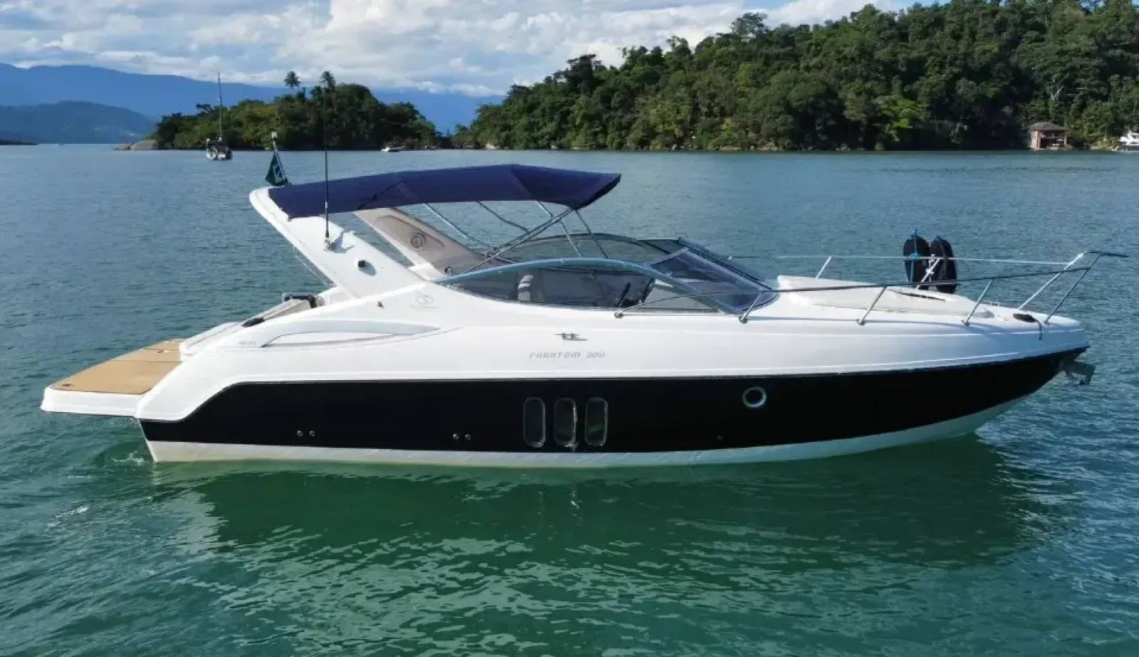 A lancha Phantom 300 da Schaefer Yachts, com casco escuro e plataforma de madeira na popa, parada em águas calmas em frente a uma margem arborizada