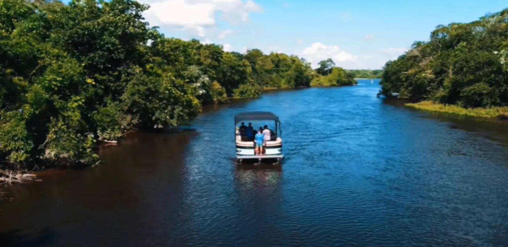 Imagem aérea de um grupo navegando de pontoon pelo Rio Baía, cercado por mata nativa, durante passeio turístico em Porto Rico-PR.
