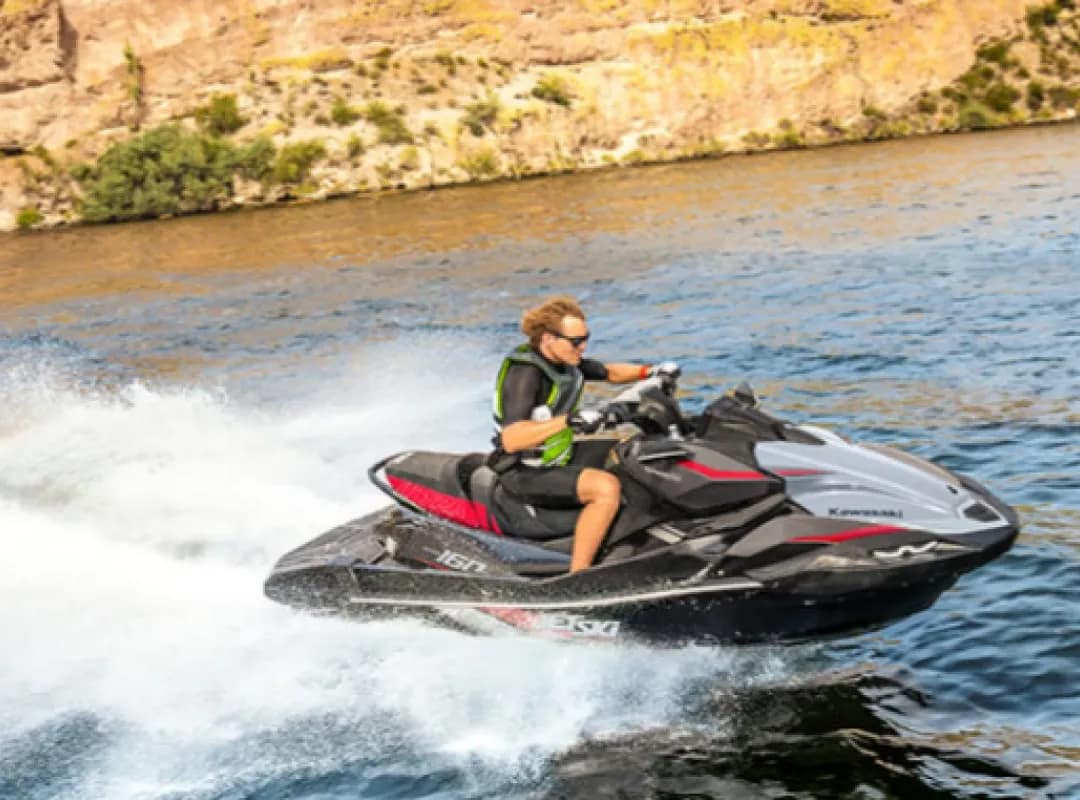 Homem dirigindo um Jet Ski Kawasaki ULTRA 160LX-S em alta velocidade em águas escuras e no fundo se vê um banco de pedras.